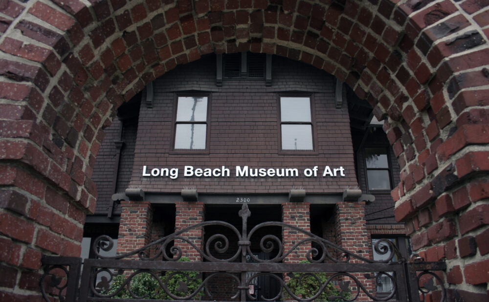 Brick archway framing the entrance of the Long Beach Museum of Art, with a wrought‑iron gate in the foreground and the museum’s name displayed on the building facade.