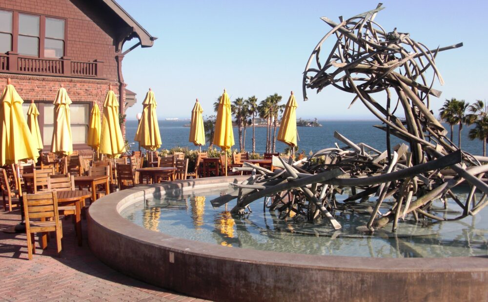 Claire's patio at sunset surrounded by wooden tables and chairs with yellow umbrellas and the Claire Falkenstein fountain