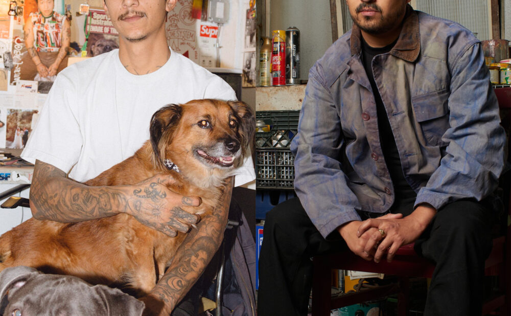 A split portrait of two artists in their workspaces. On the left, Mario Ayala, sits in a studio filled with posters, drawings, and colorful artwork, holding a brown dog on his lap while a gray dog sit in the foreground. On the right, Alfonso Gonzalez Jr. sits on a stool in an industrial studio, wearing a blue paint-marked work jacket, with spray paint cans, stacked milk crates, and art materials behind him.