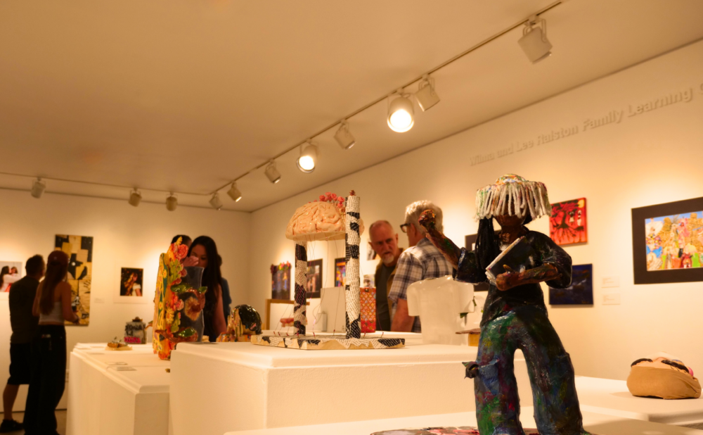 Visitors viewing sculptures and framed artwork inside an art gallery