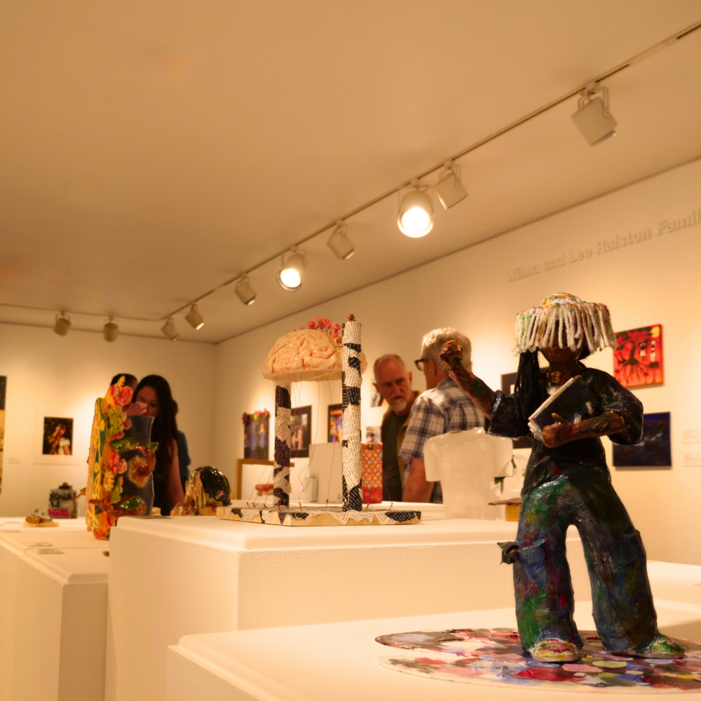 Visitors viewing sculptures and framed artwork inside an art gallery