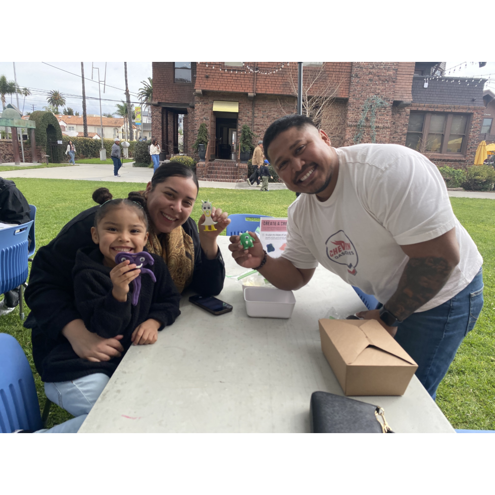 A family participating in LBMA's Family Artmaking, smiling and holding their completed art projects.