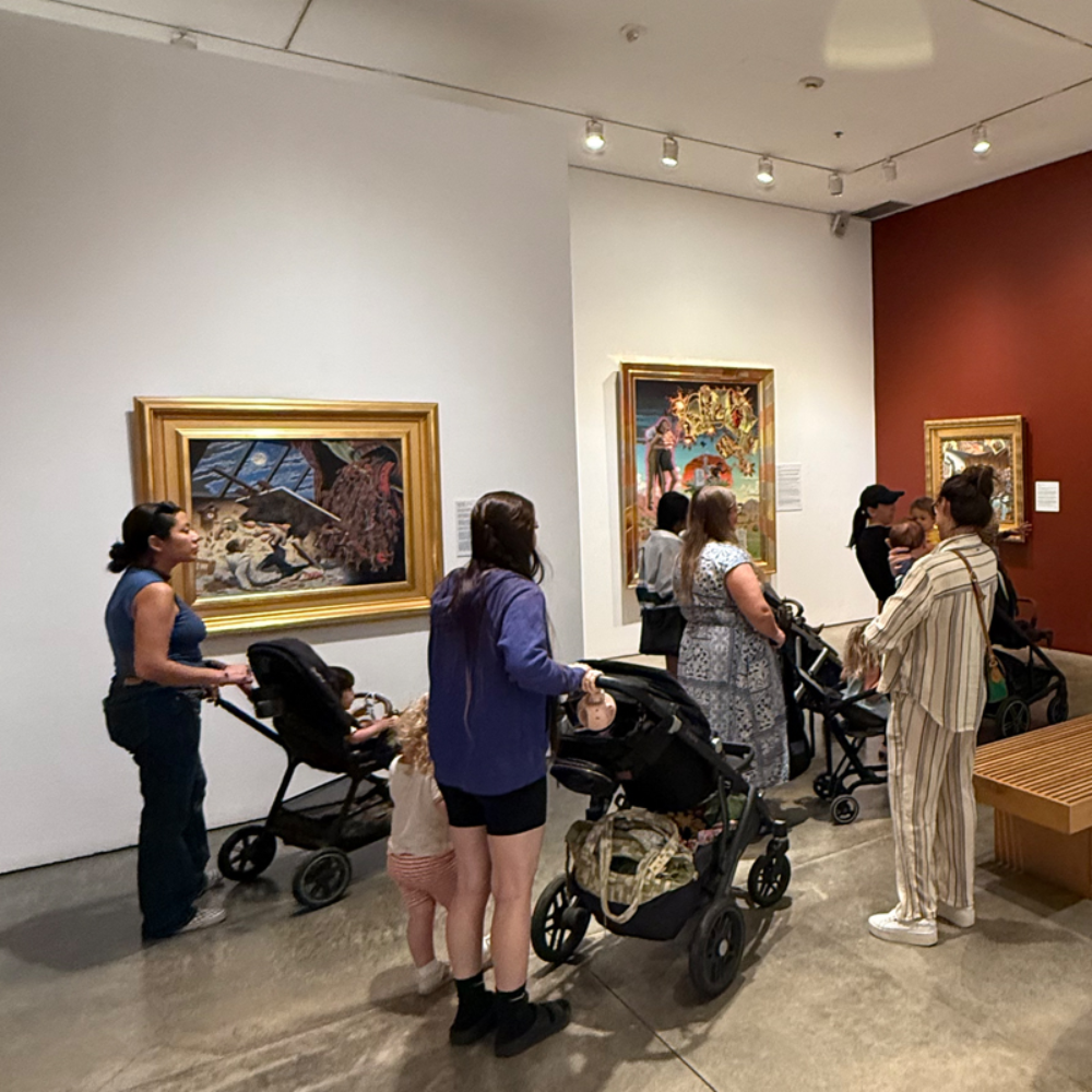 Visitors with strollers and young children explore the galleries during Stroller Tours at LBMA, viewing framed paintings on display.