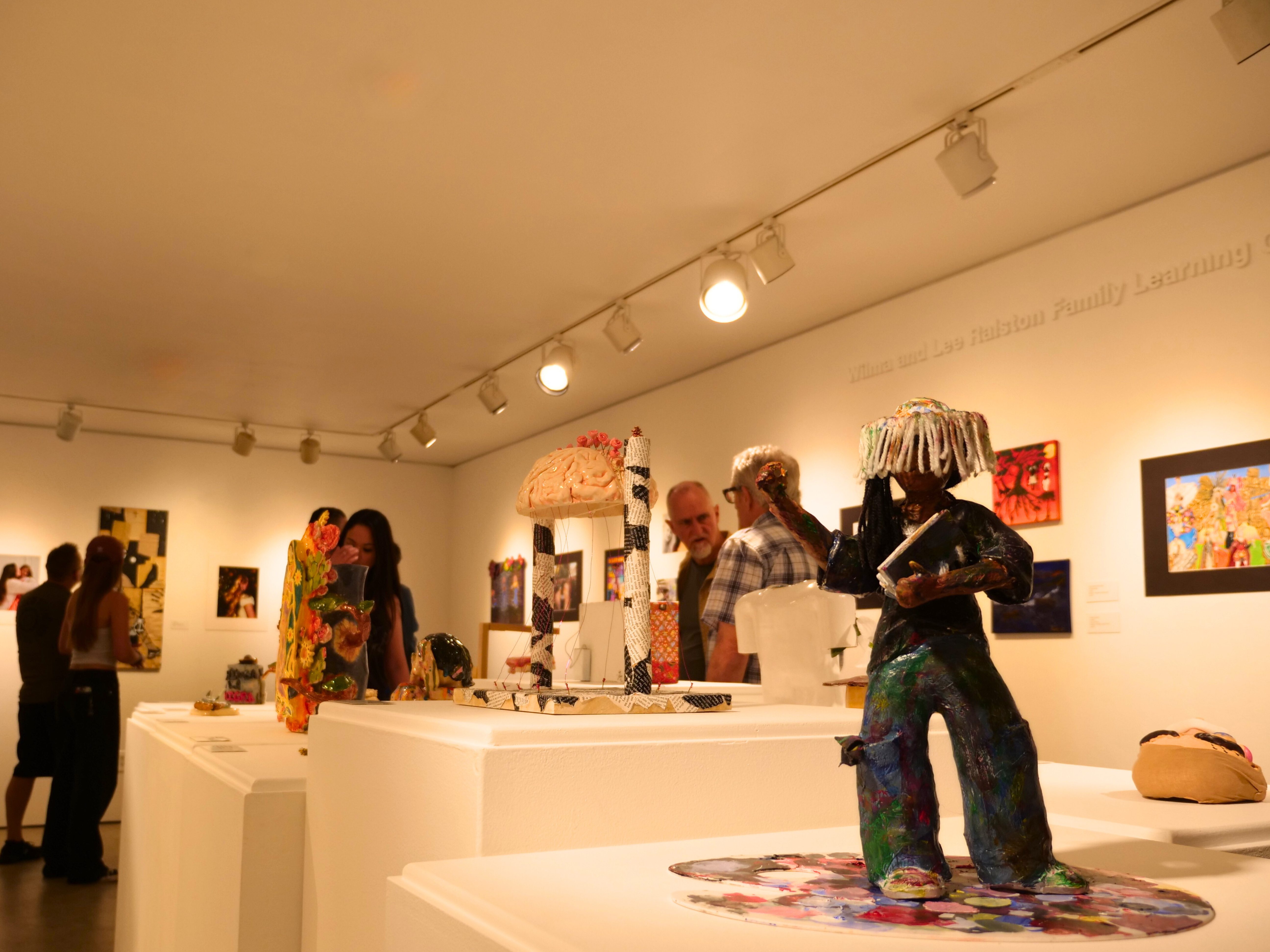 Visitors viewing sculptures and framed artwork inside an art gallery